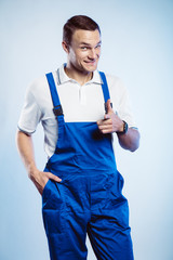 Portrait of young worker man wearing blue uniform. Pointing finger at you looking at camera. Isolated on grey background with copy space. Human face expression, emotion. Business concept.