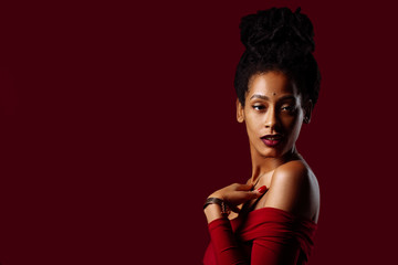 Studio portrait of a woman with dreadlocks wearing a red dress in a studio portrait on red background