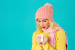© Carlos David - Cold and flu season- portrait of a sick woman in hat and scarf holding tissue, isolated on blue