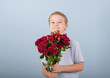 © klavdiyav - boy with a bouquet of red roses, portrait of a cute boy in a blue polo on a blue background, greeting and gift for Mother's day or Valentine's day