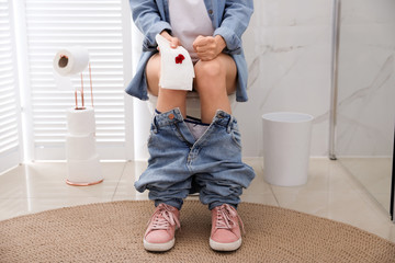 Wall Mural - Woman holding toilet paper with blood stain in rest room, closeup. Hemorrhoid concept