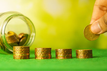 Hand Put Coins On Stacked Money. Money Stack Step Up With Blurry Coins In Bottle Against Blurry Nature Background. Financial Business Investment Concept. Free Copy Space For Text