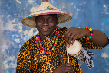 Wall Mural - African man in traditional clothes and fulani hat playing on talking drum