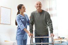 Care Worker Helping Elderly Man With Walker In Geriatric Hospice