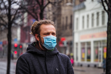 Handsome young European man in winter clothes on the street with a medical face mask on. Closeup of a 35-year-old male in a respirator to protect against infection with influenza virus or coronavirus