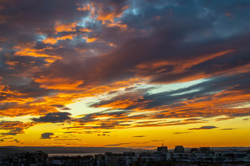 Wall Mural - sunset fire in the sky over a small city. dark blue clouds with golen reflections of the setting sun