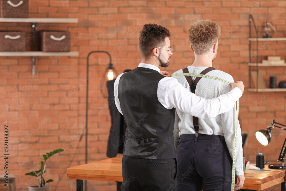Male tailor taking client's measurements in atelier