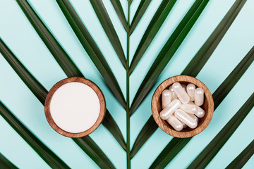 Wall Mural - Collagen in capsules and in powder in two wooden bowls on tropical leaf background