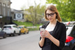 © hbrh - Woman texting while waiting for taxi bus. Half length body woman girl looking at cell phone mobile interest smile on face outdoors city urban cars on background