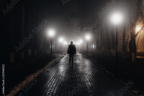 Cuadros en Lienzo Sad man alone walking along the alley in night foggy park