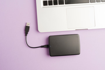 black external hard drive, partial laptop view, purple background office concept top view