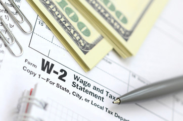 The pen, notebook and dollar bills is lies on the tax form W-2 Wage and Tax Statement. The time to pay taxes