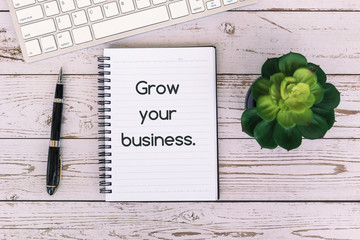 Wall Mural - Grow your business text on notepad on top of wooden table, with computer keyboard, pen and potted plant