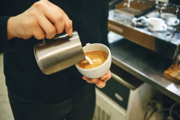 Wall Mural - Barista pours milk or cream into coffee and draws a drawing on the foam.