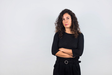 Curly hair brunette woman and black shirt with arms crossed and looking serious at the camera.