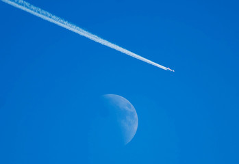 Wall Mural - Airplane- commercial aircraft- and moon in daytime.  The plane flies in the blue sky leaving a trail on the background of the moon.