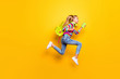 Full size profile side photo kid jump run runner hurry fast lesson hold smartphone headset backpack striped suspenders overalls sweater denim jeans isolated bright shine yellow color background