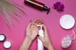 woman's hands is getting cream from dispenser close up on pink background