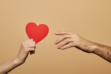 Wall Mural - cropped view of woman holding red heart and man reaching it isolated on beige