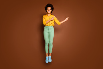 Canvas Print - Full length photo of funny dark skin lady jump high up directing fingers empty space low prices shopping wear yellow shirt green pants footwear isolated brown color background