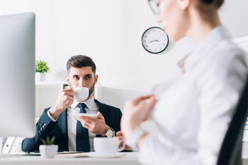 Wall Mural - selective focus of businessman drinking coffee and looking at secretary in office