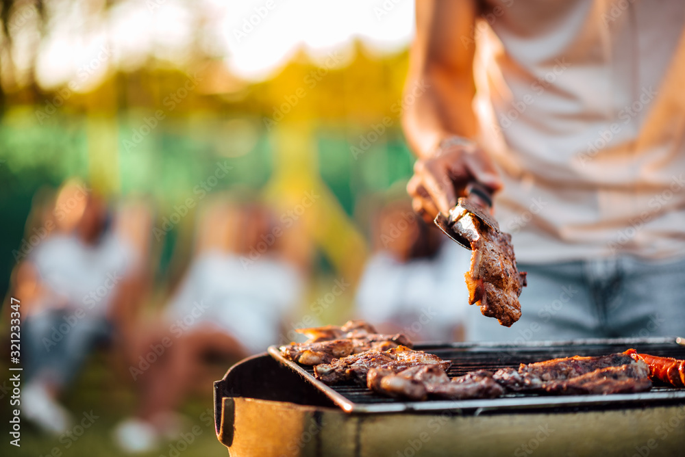 Close-up image of man barbecuing meat on the grill outdoors. - obrazy, fototapety, plakaty 