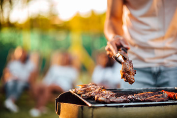 Close-up image of man barbecuing meat on the grill outdoors.