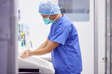 Wall Mural - Male Surgeon Wearing Scrubs Washing Hands Before Operation In Hospital Operating Theater