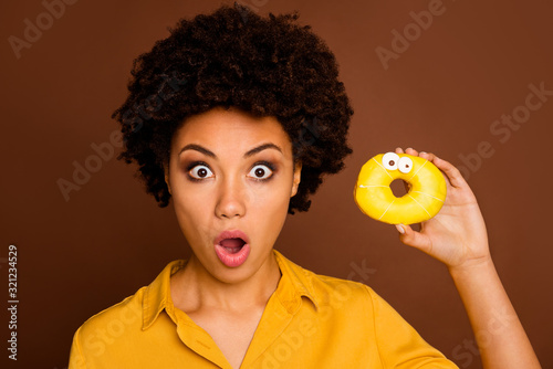 This cake can speak. Closeup photo of shocked dark skin lady hold colorful donut caramel eyes human face painting wear yellow shirt isolated brown color background