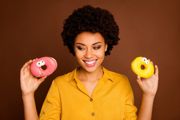 Closeup photo of funky dark skin lady hold two colorful donuts caramel eyes human faces painting choose what to eat first wear yellow shirt isolated brown color background