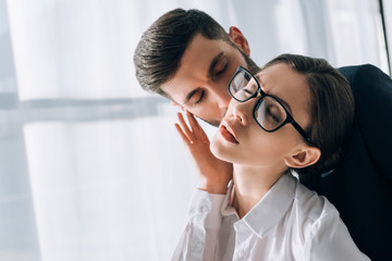 Wall Mural - businessman kissing attractive secretary with closed eyes in office