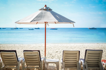 White beach umbrellas on the beach against the blue sky and blue sea background on sunny day. Summer vacation and holiday concept.