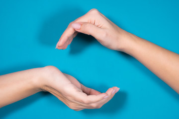 Closeup top view flatlay photography of two rounded manicured female hands isolated on blue background with empty copyspace in middle between palms.