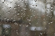Krople deszczu na szybie, w tle nieostry zarys domu.
