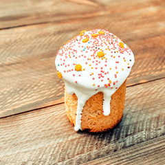 Happy Easter cake with sprinkles on white glaze. Easter cake on old rustic wooden board, lace cloth. Festive homemade bakery, spring holiday preparation. Selective focus, free text space. 