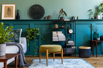 Interior design of living room with gray sofa, design pouf, wooden cube, shlef and elegant personal accessories. Green wood panelling with shelf. Modern home decor. Mock up poster frame. Template