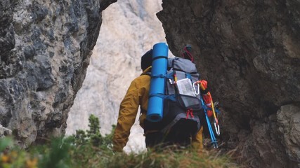 Wall Mural - young man hiker hiking under mountain narrow passage. yellow jacket, backpack, black beard and beani