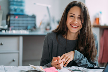 Portrait of smiling cute hipster girl staring on camera while writing college exercises in notebook.