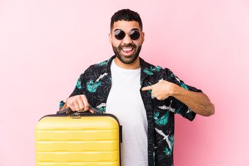 Wall Mural - Young latin man holding a suitcase surprised pointing at himself, smiling broadly.