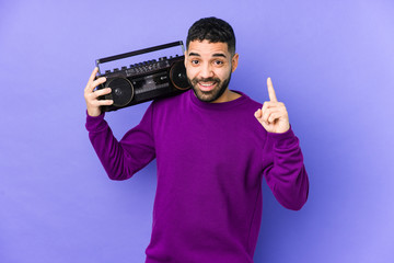 Wall Mural - Young arabian man holding a radio cassette isolated Young arabian man listening music having an idea, inspiration concept.