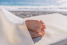 Closeup View Of Cute Small Bare Feet O Little Caucasian Child Sleeping At Sunny Beach Calmly. Legs Covered With Soft Towel.