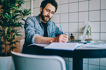 Male remote worker taking notes and using laptop