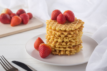 Wall Mural - Delicious waffles with fresh fruit and berries on a white wooden table. Waffles with strawberries and blueberries. Free space for text. Traditional belgian waffles with fresh fruit. Stack of waffles w