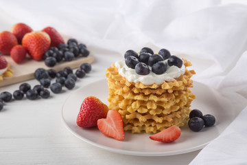 Wall Mural - Delicious waffles with fresh fruit and berries on a white wooden table. Waffles with strawberries and blueberries. Free space for text. Traditional belgian waffles with fresh fruit. Stack of waffles w