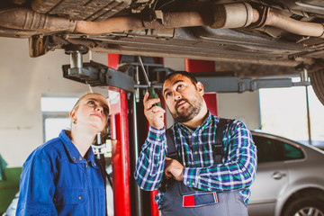 Mechanic man examining car with trainee girl