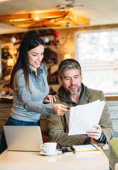 Portrait of young business man and woman at cafe discussing contract.