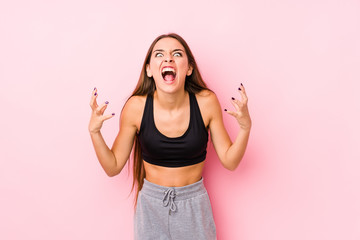 Wall Mural - Young caucasian fitness woman posing in a pink background screaming with rage.