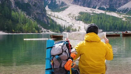 Wall Mural - young tourist hiker man reading map sitting by alpine lake lago di braies (pragser wildsee) in trent