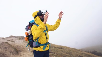 Wall Mural - vr virtual reality headset. young man hiker moving hands on cloudy sky and fog background. yellow ho