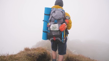 Wall Mural - young man hiker on mountain with cloudy sky and fog. yellow jacket, backpack and beanie. traveling d